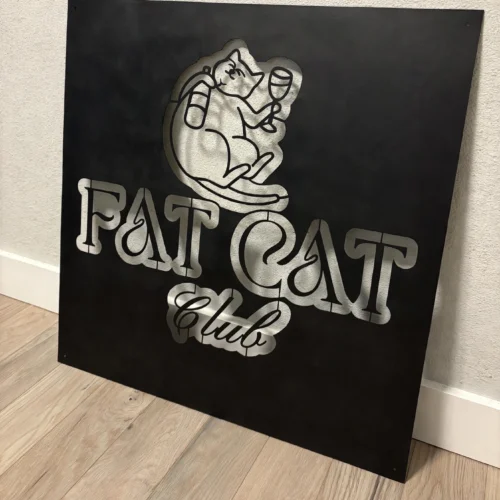 Fat Cat Club custom metal logo sign, leaning against a wall on a light oak floor