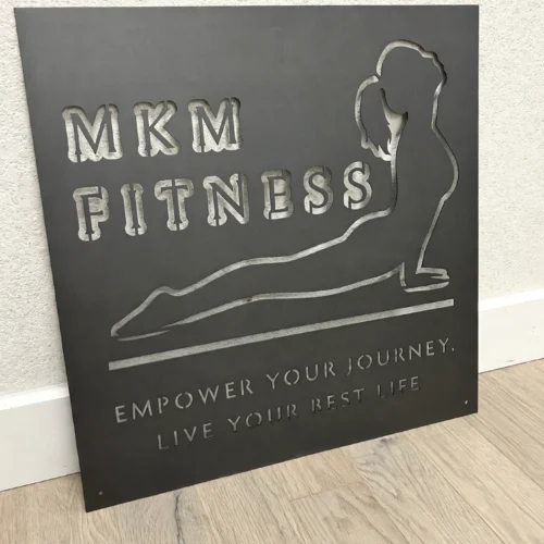 MKM Fitness business logo sign, leaning against a wall on a light oak floor